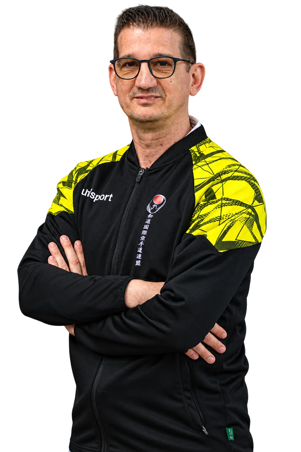 Sandro Cammarata, sensei du Cobra Kaï, en veste du club, les bras croisés.